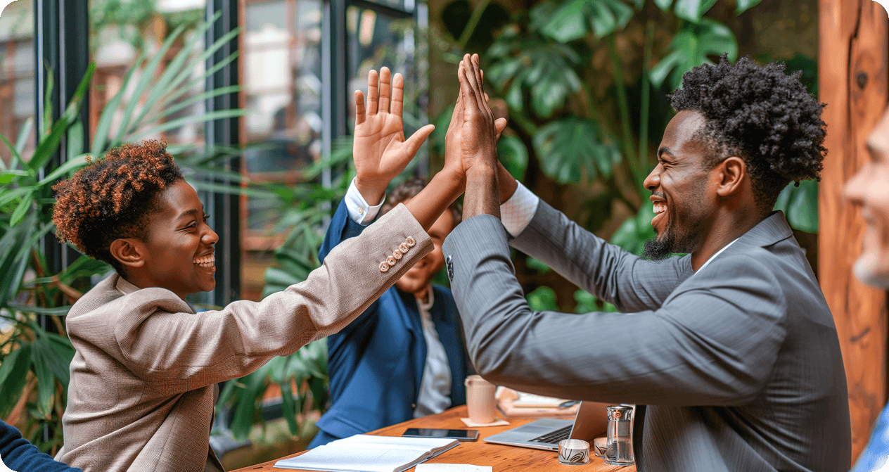 Two smiling colleagues sharing a high five across a meeting table